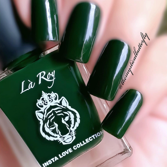 A close-up of a hand with glossy dark green nail polish, shown next to a bottle of La Roy Insta Love Collection nail polish in the same deep green shade.